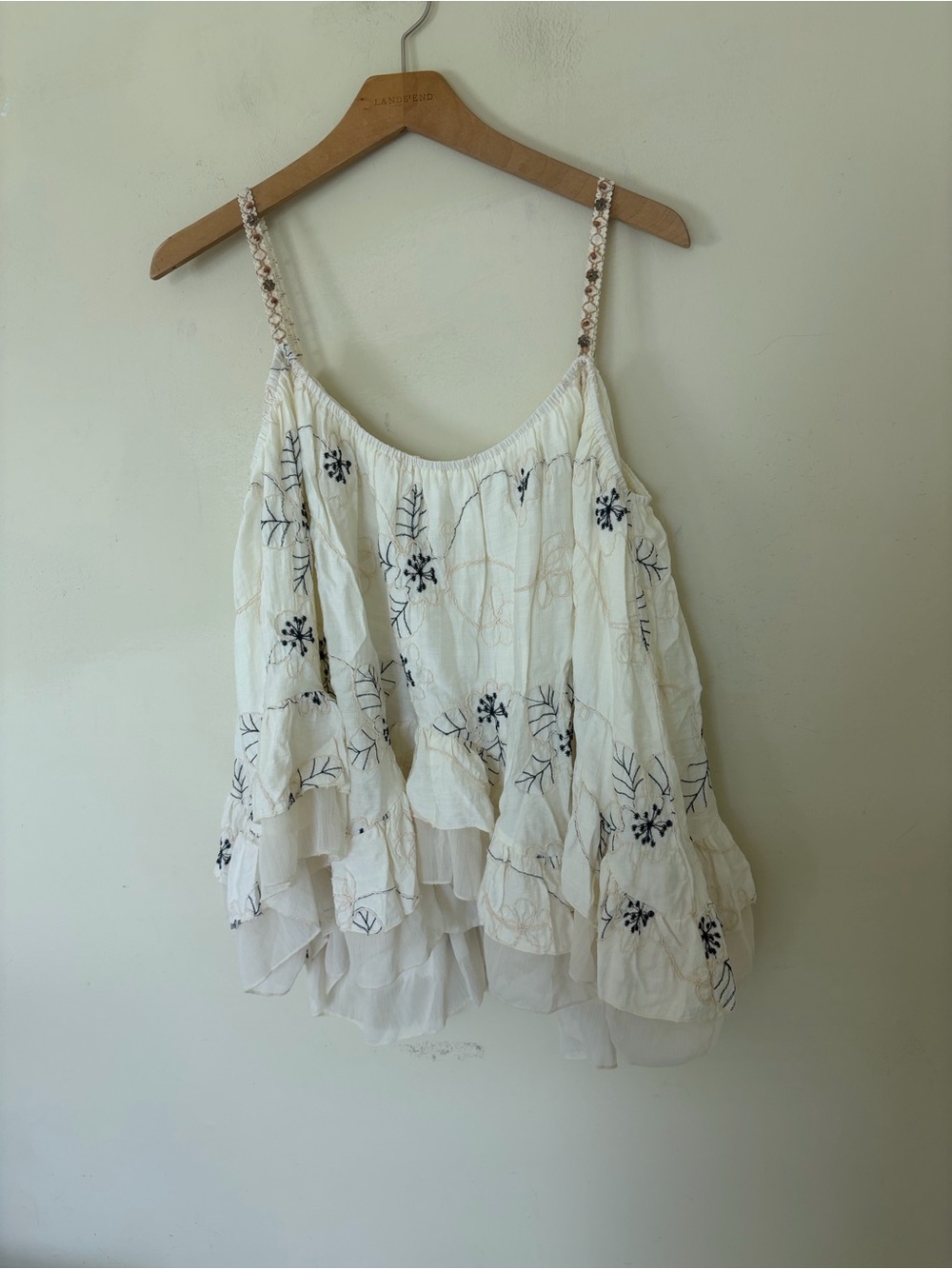 Boutique white camisole features intricate black floral embroidery and delicate